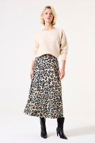 Woman standing in full view wearing the beige sweater tucked into a leopard print skirt with black boots.