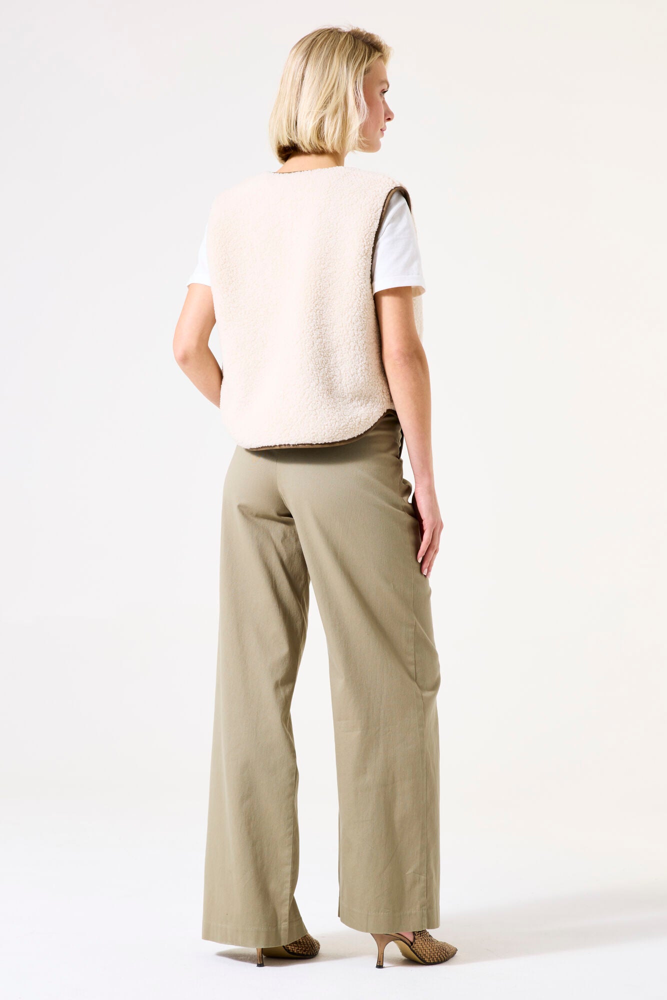Back View of Woman wearing a beige vest and pants on a white background