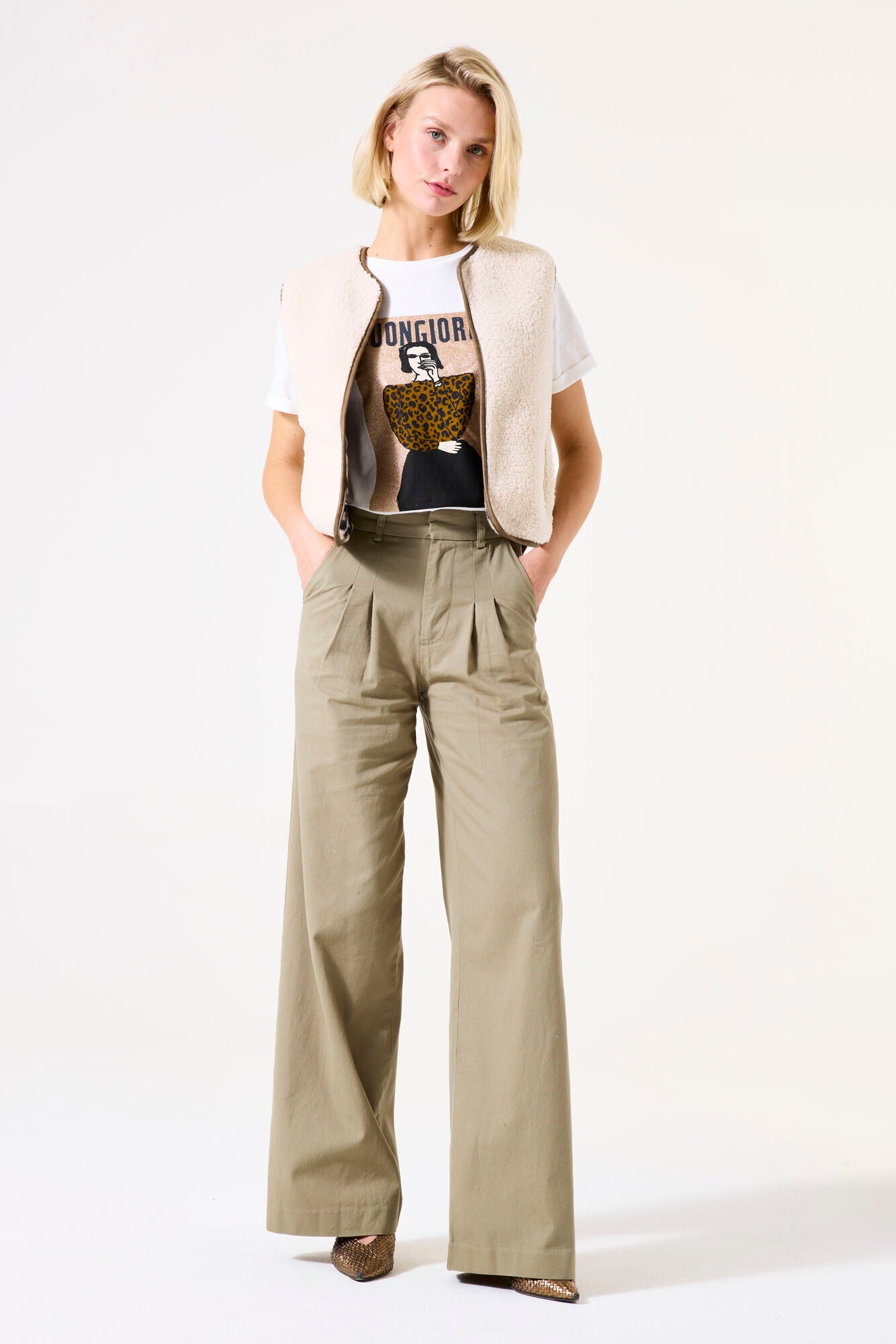 Woman wearing a beige vest over a graphic t-shirt with wide-leg pants on a white background