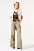 Woman wearing a beige vest over a graphic t-shirt with wide-leg pants on a white background