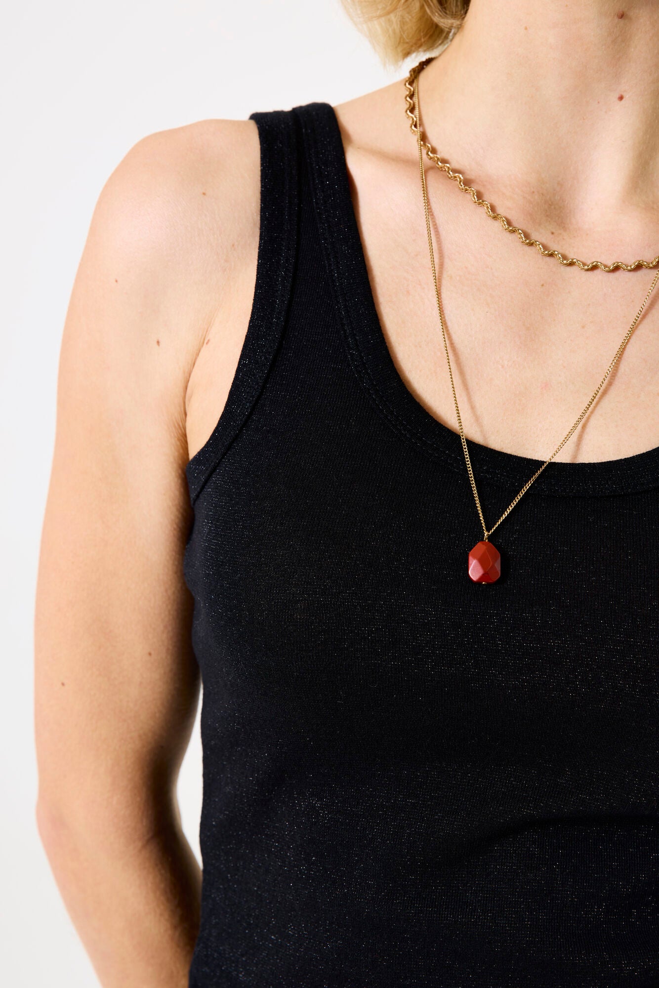 Person wearing a black tank top and gold necklace with a red pendant on a white background
