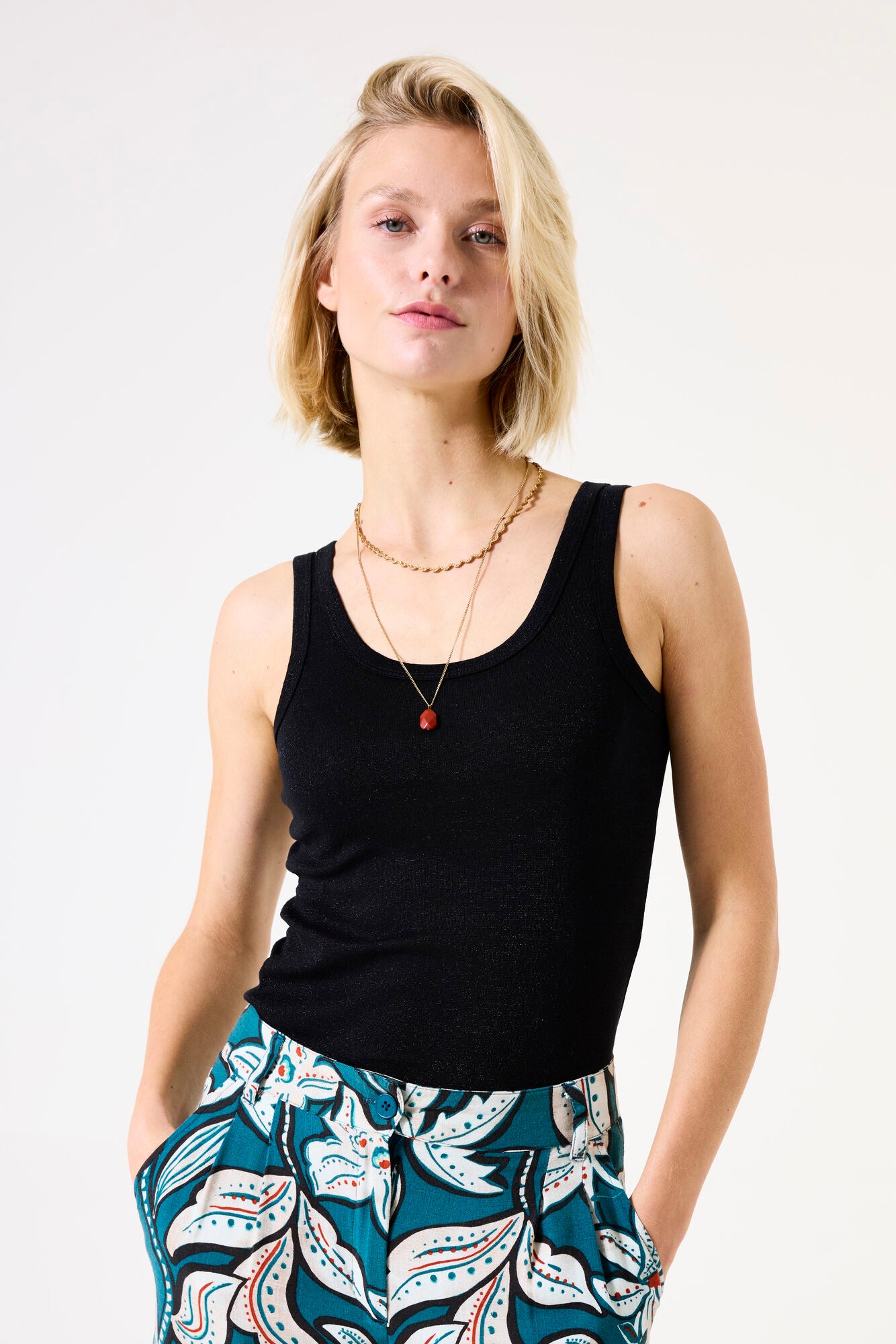 Woman wearing a black tank top and patterned pants on a white background