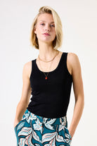 Woman wearing a black tank top and patterned pants on a white background