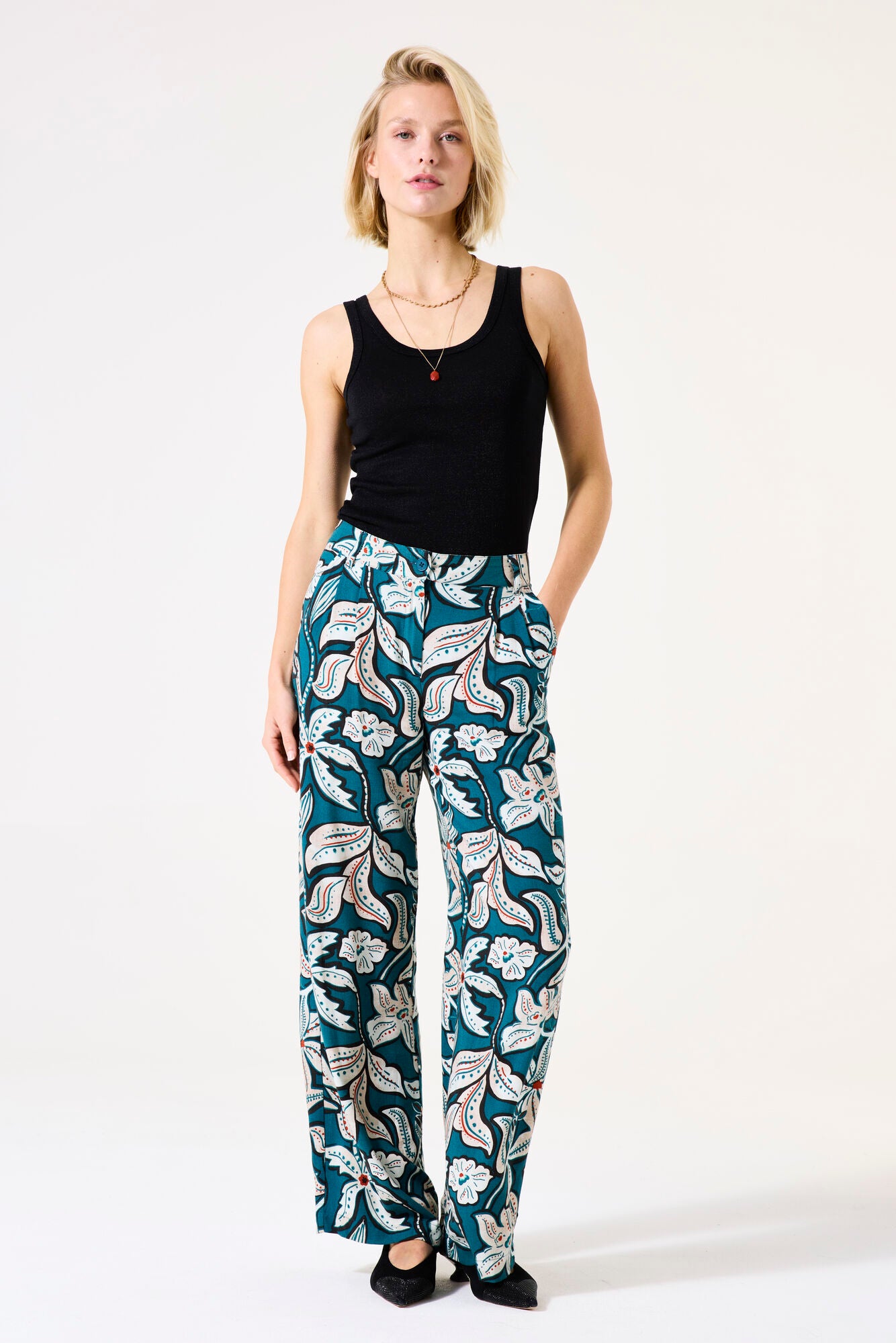 Woman wearing a black tank top and floral pants on a white background