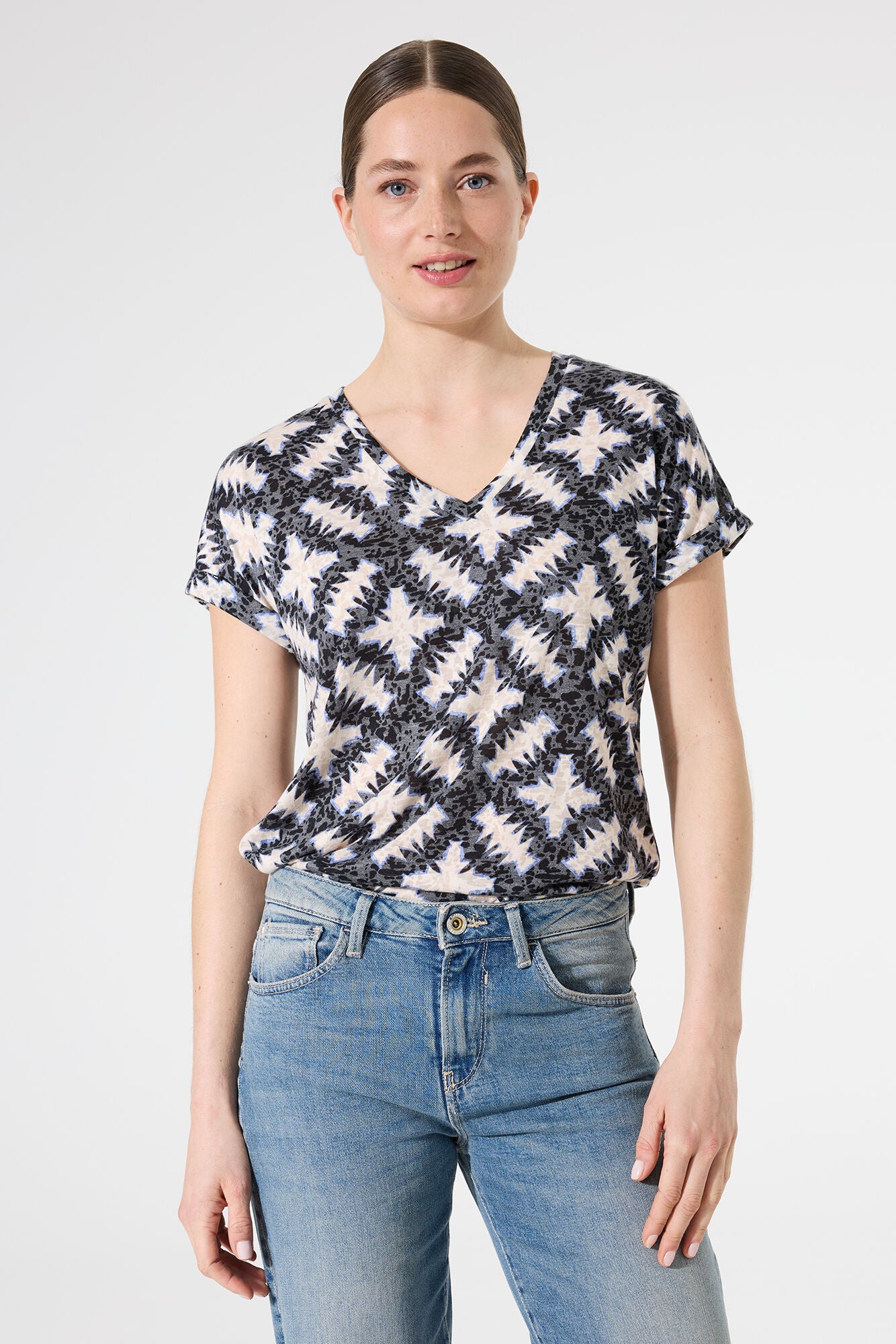Woman wearing a patterned top and jeans on a plain background