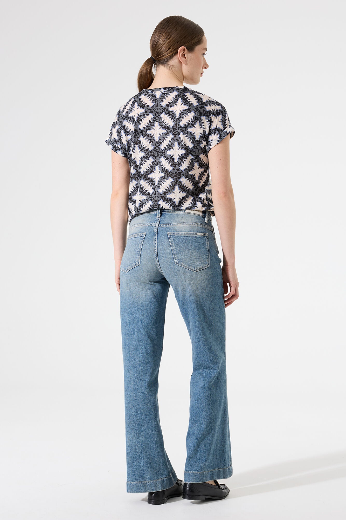 Back View of a Woman wearing a patterned top and blue jeans on a white background