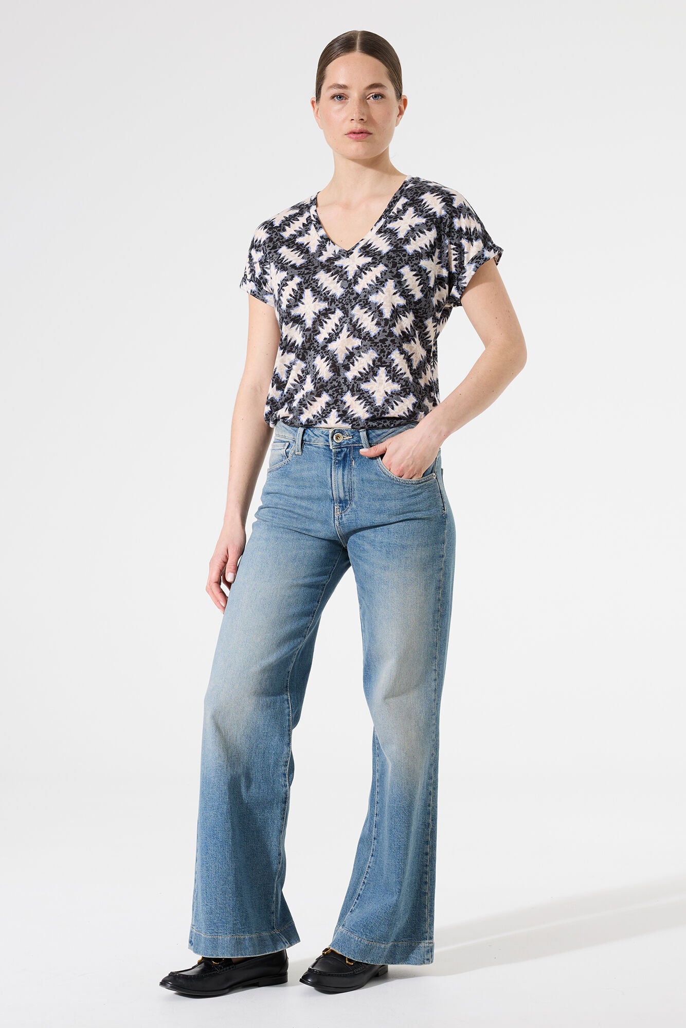 Woman wearing a patterned top and blue jeans on a white background