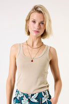 Woman wearing a beige tank top and colorful pants against a white background