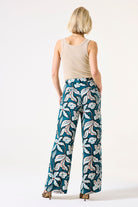 Back View of Woman wearing a beige tank top and teal floral pants on a white background
