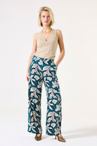 Woman wearing a beige tank top and teal floral pants on a white background