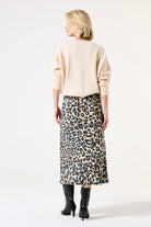 Back view of woman wearing leopard-print satin midi skirt with black heeled boots and beige sweater