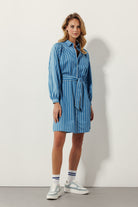 blonde woman standing with arms down in blue dress and sneakers
