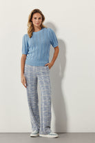 Woman wearing a light blue short sleeve open-knit sweater with puff sleeves and decorative buttons at the shoulder.