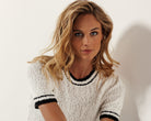 Woman wearing a short-sleeve textured white sweater with trim at the collar and cuffs, paired with patterned pants.